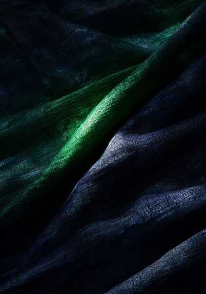Luxurious Textured Fabric Draped Luxurious dark green and navy textured fabric draped in folds, illuminated by focused light against a shadowy background.