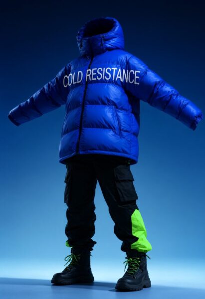 Futuristic Blue Puffer In Neon Glow A person wears a vibrant blue puffer jacket with "cold resistance" on the back, paired with black cargo pants and neon green accents, standing against a gradient blue background.