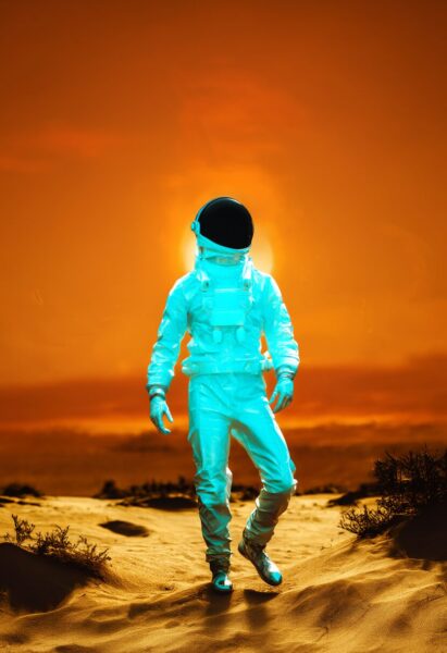 Glowing Astronaut In Desert A glowing cyan astronaut walks across sandy dunes under an orange sunset sky.