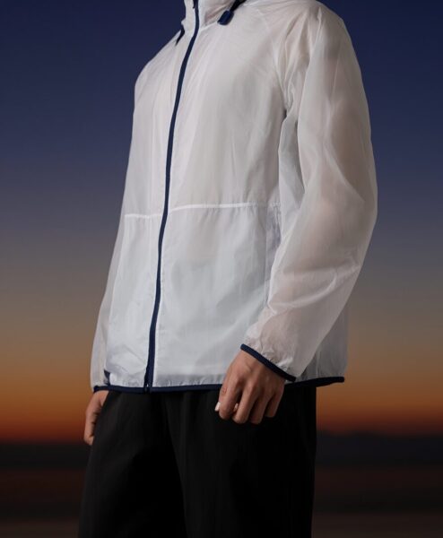 Transparent Windbreaker Over Black Pants Person in white transparent windbreaker with navy trim over black pants at sunset horizon.
