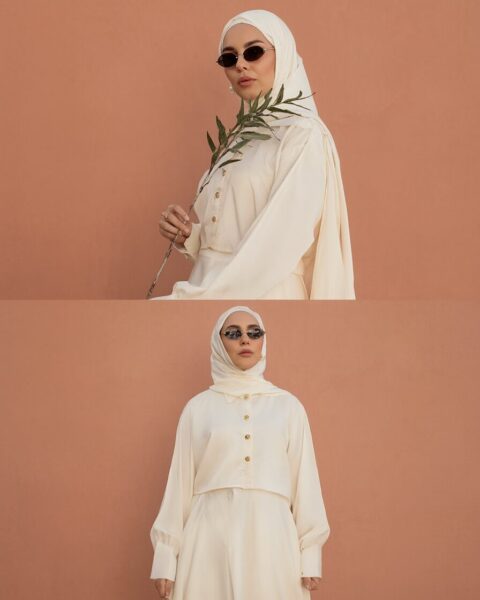 Elegant Modest Attire In Soft Ivory A woman wearing elegant ivory modest attire with a hijab, holding olive branch against terracotta background.