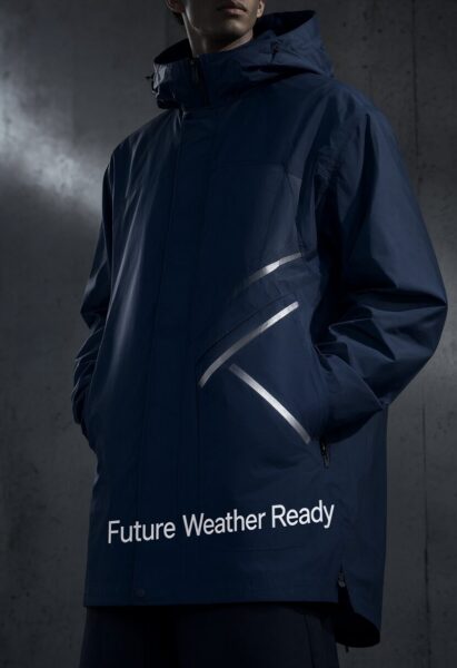 Urban Tech Jacket In Midnight Blue A person wears a midnight blue urban tech jacket with reflective stripes and "future weather ready" text, standing against a concrete wall.