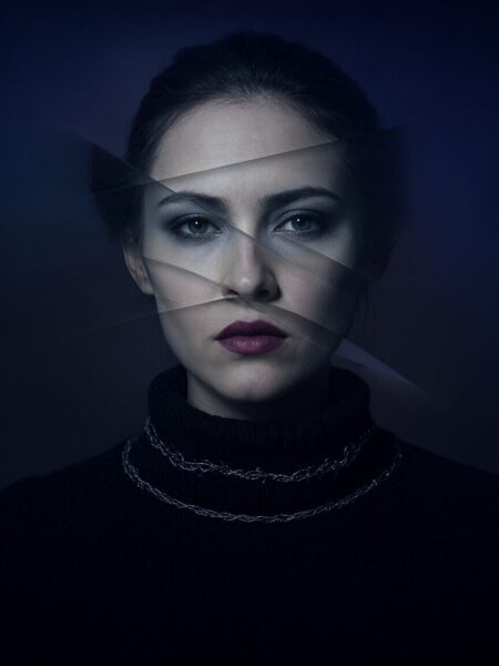 Fragmented Portrait With Crimson Lips A woman's face partially obscured by geometric shards, wearing a black turtleneck and silver chain, against a deep blue background.