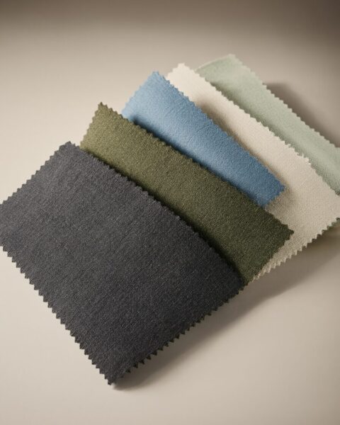 Textured Fabric Swatches In Earth Tones Five textured fabric swatches in earthy tones including gray, olive green, blue, cream, and sage green arranged diagonally on a neutral background.