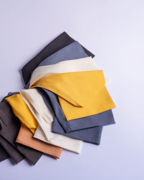 Textured Fabric Swatches In Soft Palette Stacked textured fabric swatches in muted tones including gray, beige, mustard yellow, and terracotta against a light purple background.