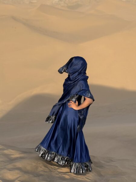 Ethereal Desert Drifter A person wearing a flowing royal blue dress with silver trim stands alone on golden desert sands under warm sunlight.