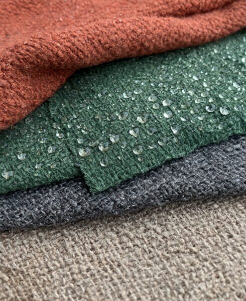 Textured Fabrics With Raindrops Stacked textured fabrics in earthy tones with water droplets resting on their surfaces, showcasing durability and weave details.