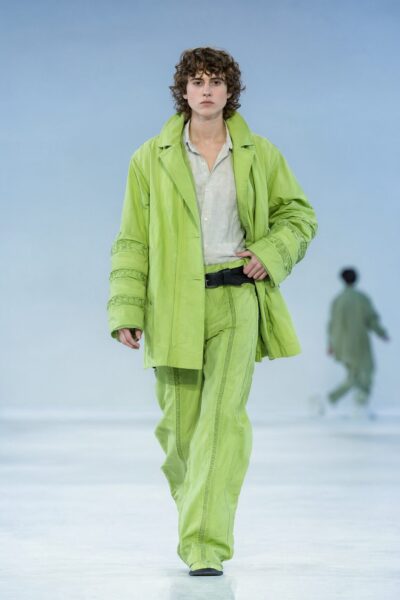 Model Strides In Lime Ensemble Model walks confidently down a runway wearing an oversized lime green jacket and matching pants with a black belt.
