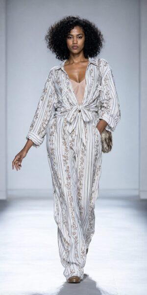 Model Striding In Floral Striped Loungewear Model strides confidently down a white runway wearing a loose-fitting floral striped jumpsuit with a tied waist and fur-trimmed clutch.