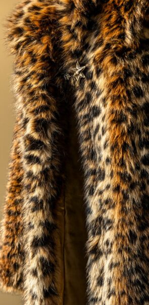 Leopard Print Fur Coat Close-Up Close-up of a luxurious leopard print fur coat featuring a silver star-shaped clasp on the sleeve against warm background lighting.