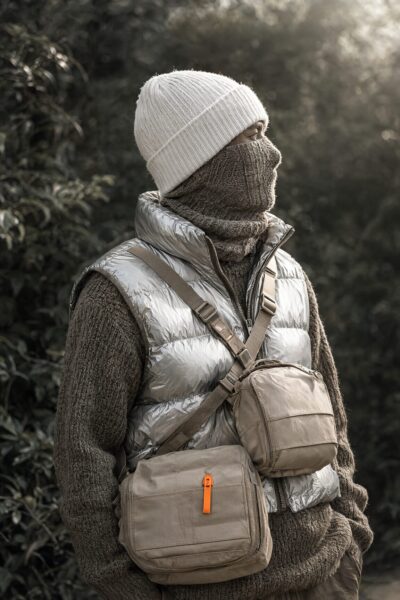 Urban Explorer In Monochrome Forest Urban explorer wearing silver vest, knit hat, and beige crossbody bags stands in monochrome forest at golden hour.