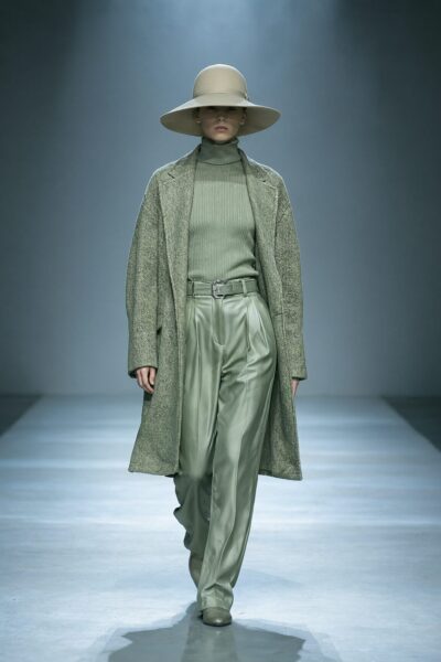 Serene Monochrome Green Ensemble Model walks down runway wearing monochrome green ensemble with wide-brimmed hat and belted coat.