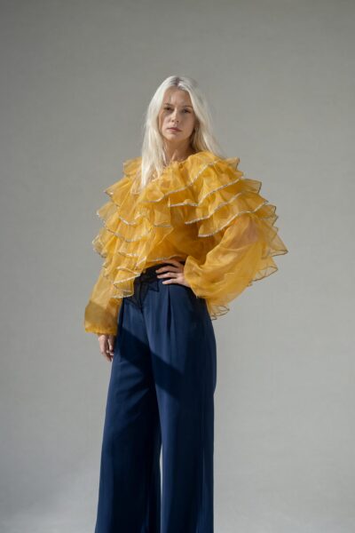 Golden Ruffles Meet Midnight Blue A woman in a golden ruffled blouse and midnight blue wide-leg pants poses against a neutral gray background.