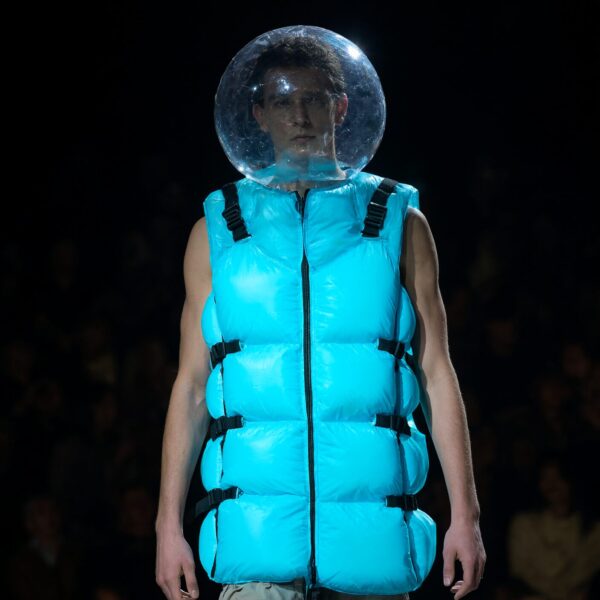Neon Vest With Floating Bubble Accent Model wears electric blue puffer vest with clear bubble helmet floating above head on dimly lit runway.