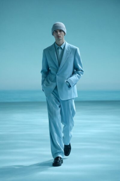 Serene Blue Monochrome Ensemble A male model walks confidently in a light blue suit and knit cap under cool-toned lighting on a minimalist runway.