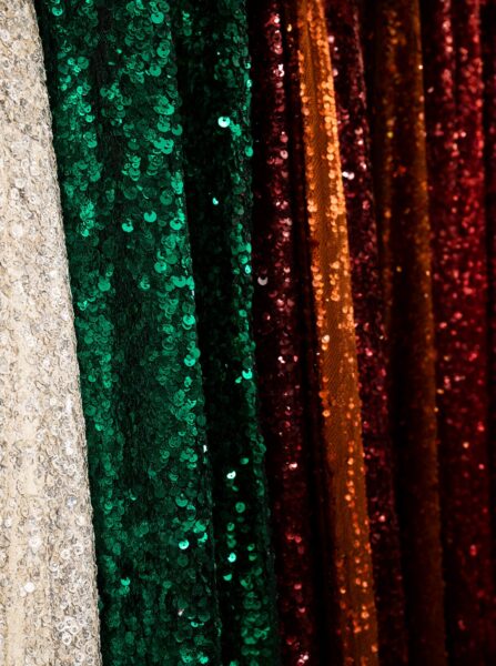 Glimmering Sequin Drapes In Twilight Hues Glimmering sequin fabric panels in cream, emerald green, red, and gold draped vertically under soft lighting.