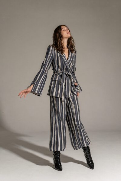 Graceful Plaid Suit In Soft Light A woman poses gracefully in a navy and cream vertical stripe suit with belt, black boots, against a neutral studio background.