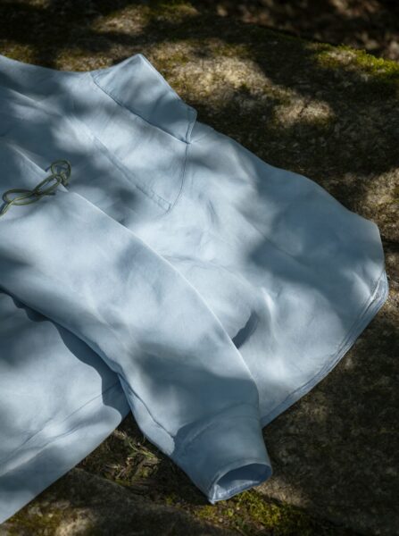 Sunlit Silk Shirt Draped In Dappled Light A light blue silk shirt draped on mossy stones, illuminated by dappled sunlight through tree leaves.