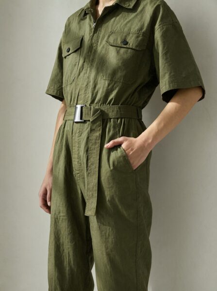 Olive Utility Jumpsuit Styled Pose Person wearing olive green utility jumpsuit with belt and pockets, standing in neutral studio lighting.