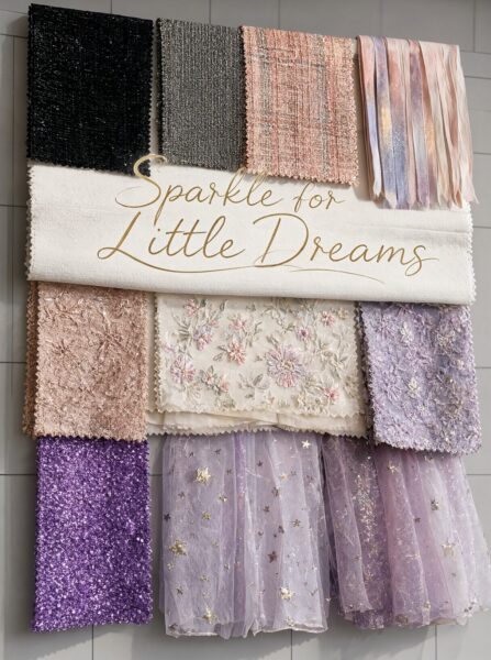 Glimmering Fabric Swatches Display A wall display of shimmering fabrics in pastel purples, pinks, and golds, arranged neatly with a golden cursive slogan reading 'sparkle for little dreams'.