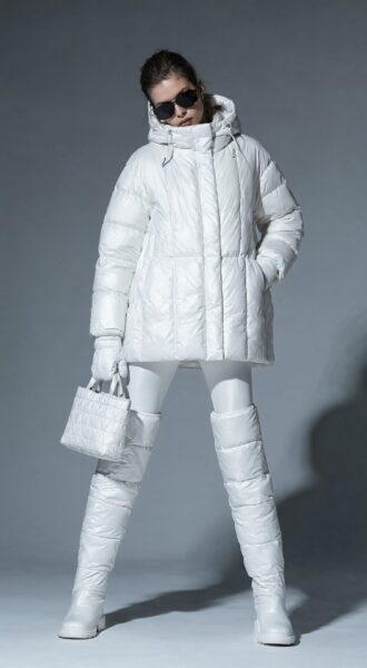 Winter Monochrome Couture Ensemble A woman in an all-white puffer coat, matching thigh-high boots, and gloves holds a white quilted bag while wearing dark sunglasses against a gray backdrop.