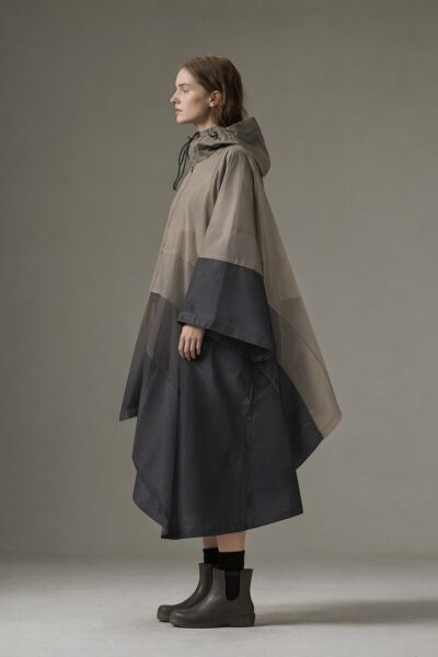 Modern Raincape With Earthy Gradient A woman in profile wears a modern earth-toned rain cape with layered panels and a hood against a neutral studio backdrop.