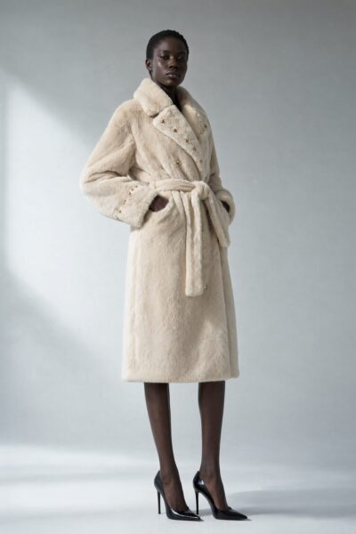 Cream Fur Coat With Crystal Accents A model wears a cream-colored fur coat with gold-tone buttons and belt against a neutral studio background.