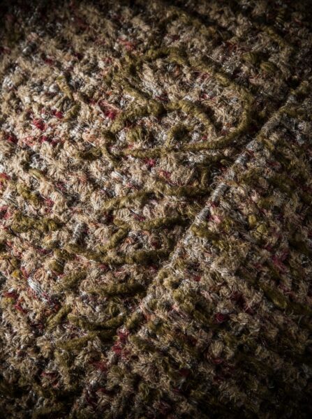 Textured Patchwork Jacket Close-Up Close-up of textured patchwork fabric in earthy browns, greens, and reds with frayed yarn details.