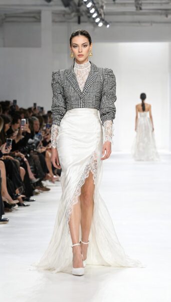Elegant Runway Model In Houndstooth Ensemble Elegant model walks runway in houndstooth blazer, lace blouse, and high-slit satin skirt with white heels.