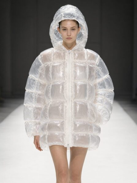 Model In Transparent Inflatable Jacket Model walks down runway wearing an oversized transparent inflatable hooded jacket with grid-patterned chambers.