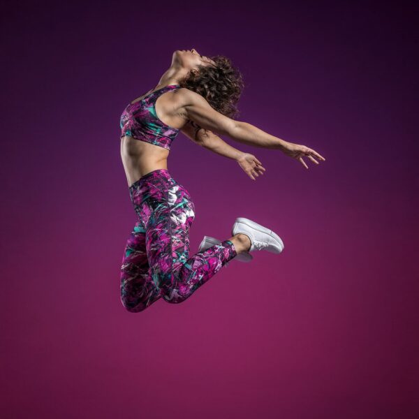 Dynamic Jump Against Gradient Sky A woman in colorful athletic wear leaps dynamically against a purple-to-pink gradient backdrop, showcasing energetic movement.