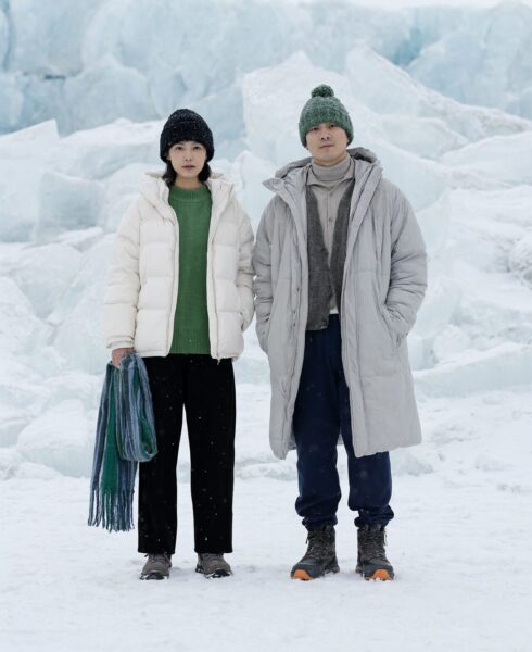 Winter Duo Amidst Glacial Ice A man and woman stand side-by-side in snowy terrain wearing winter coats, beanies, and scarves against a backdrop of massive ice blocks.
